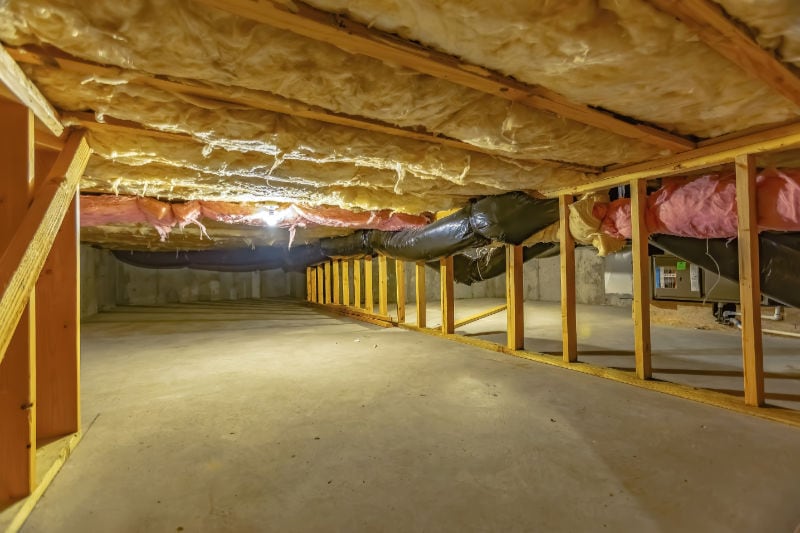 Basement crawl space with upper floor insulation and wooden support beams.