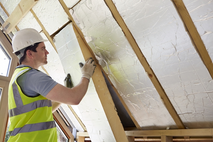 Builder Fitting Insulation Into Roof Of New Home